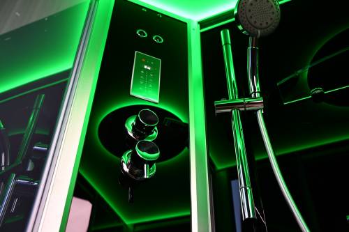 Shower control panel with green lighting and shower head in a dark setting