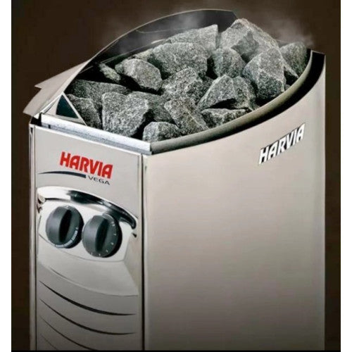 A Harvia VEGA stone heater with gray heating stones visible inside, featuring a brushed silver metal body and red and black Harvia branding.