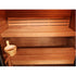 A wooden double-tier sauna bench with a small wooden bucket and ladle placed on the lower bench, shown against a warm wood interior.